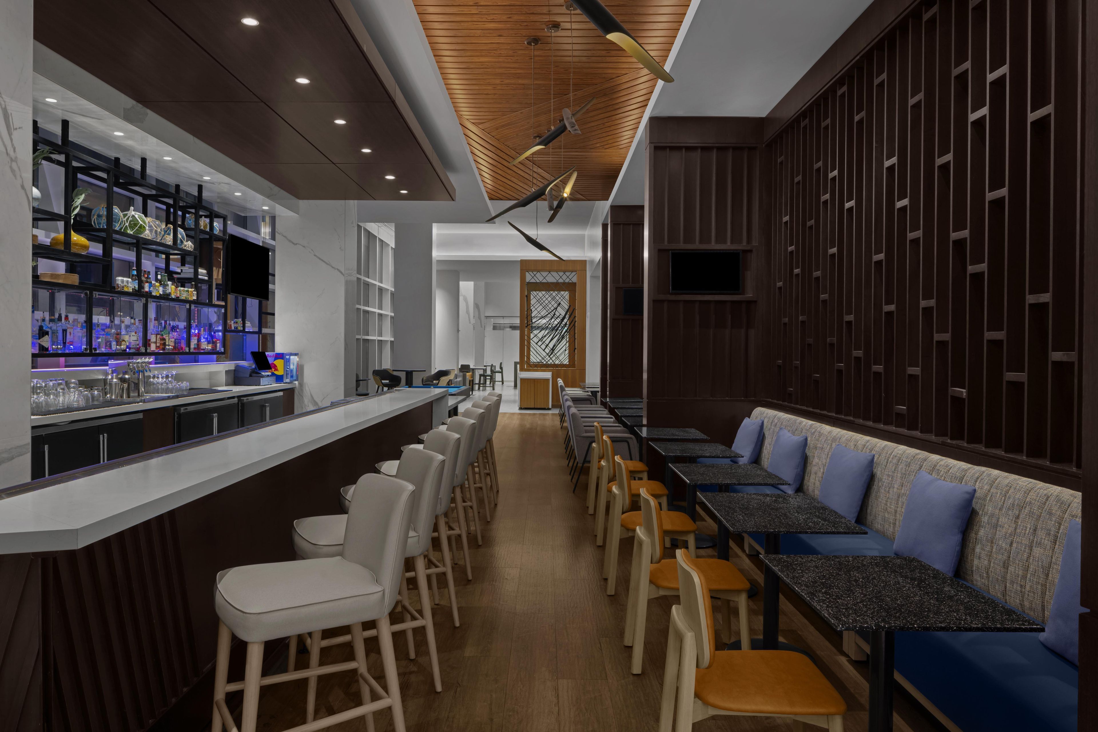 A modern bar area with a long counter, bar stools, and a seating area with tables and chairs.