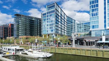 A modern waterfront hotel with a glass facade, a dock with a boat, and a pedestrian walkway.