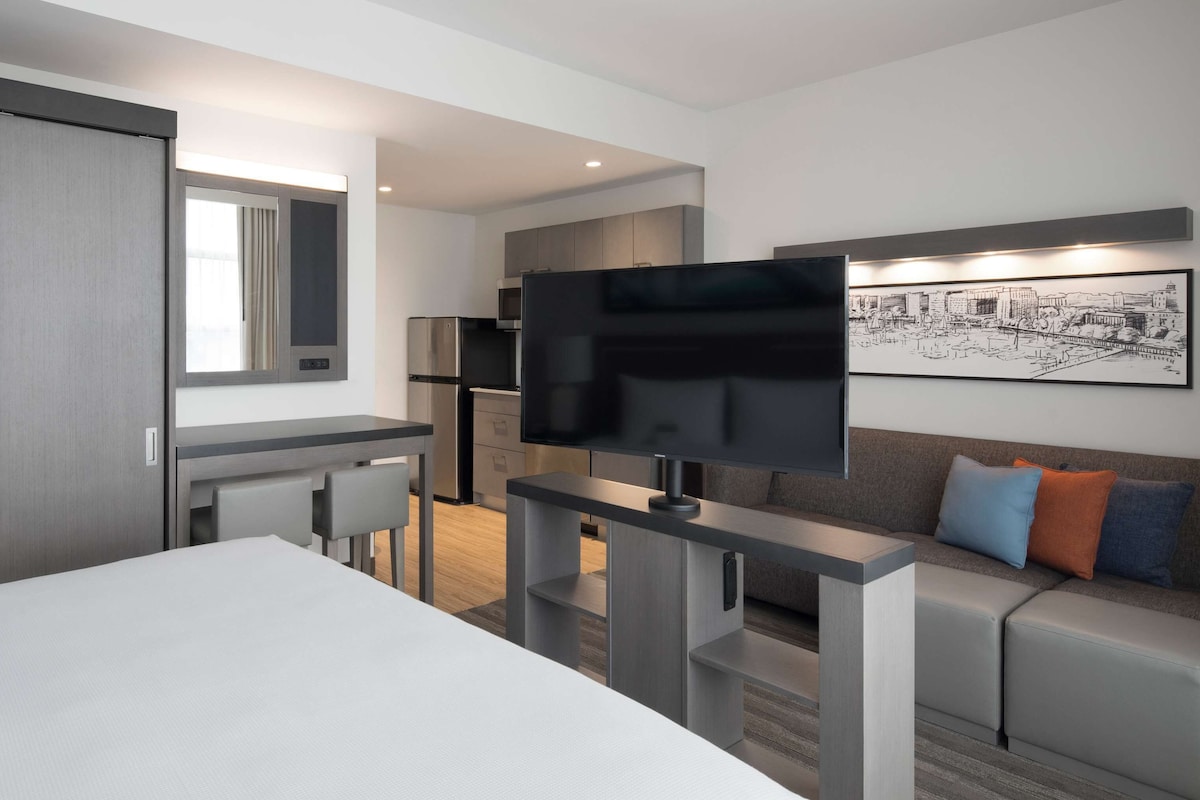 Una habitación de hotel moderna con una cama, un escritorio, un televisor y un sofá.