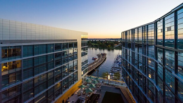 A modern building with a glass facade overlooking a river with boats.