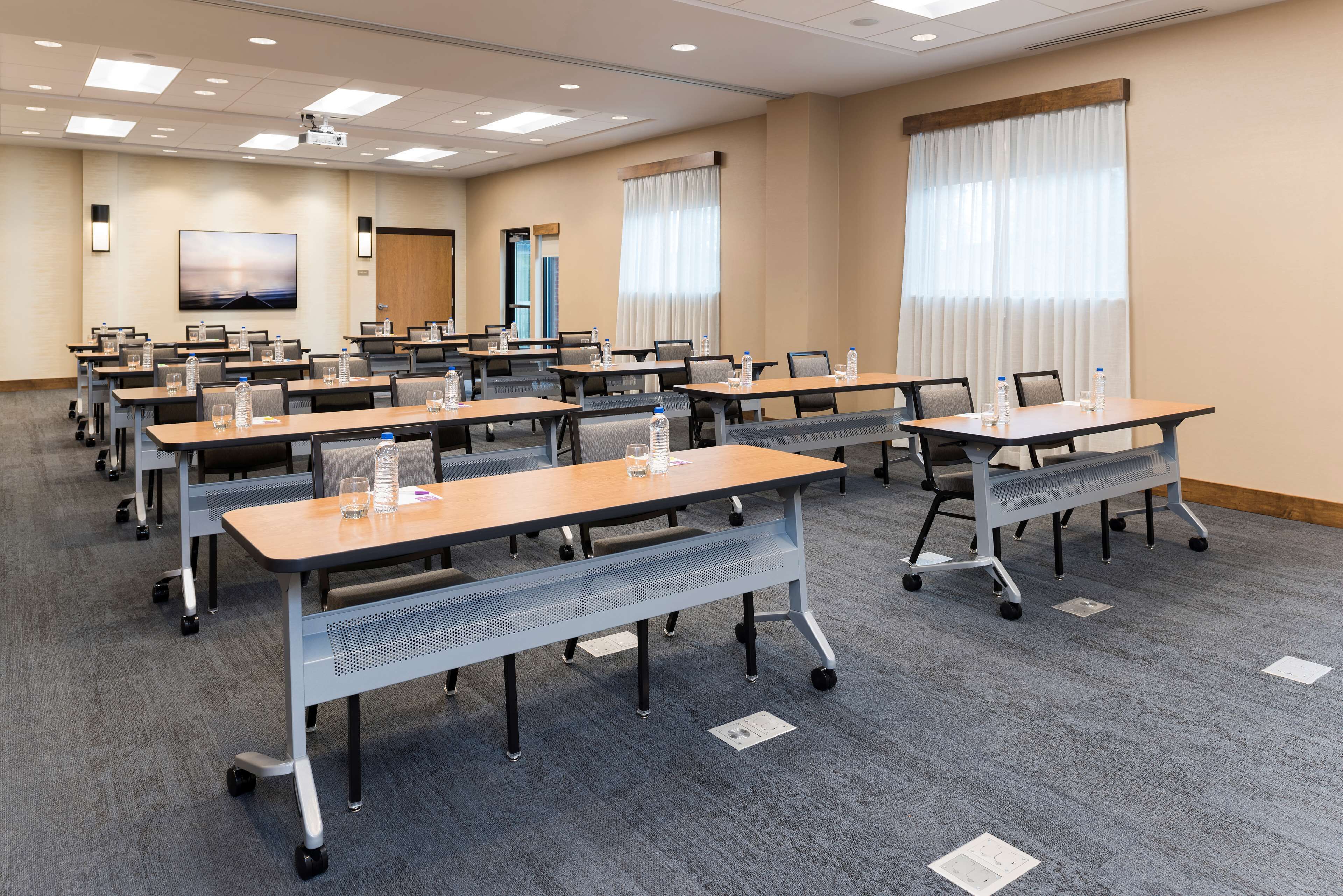 A conference room with multiple tables, chairs, and a projector screen.