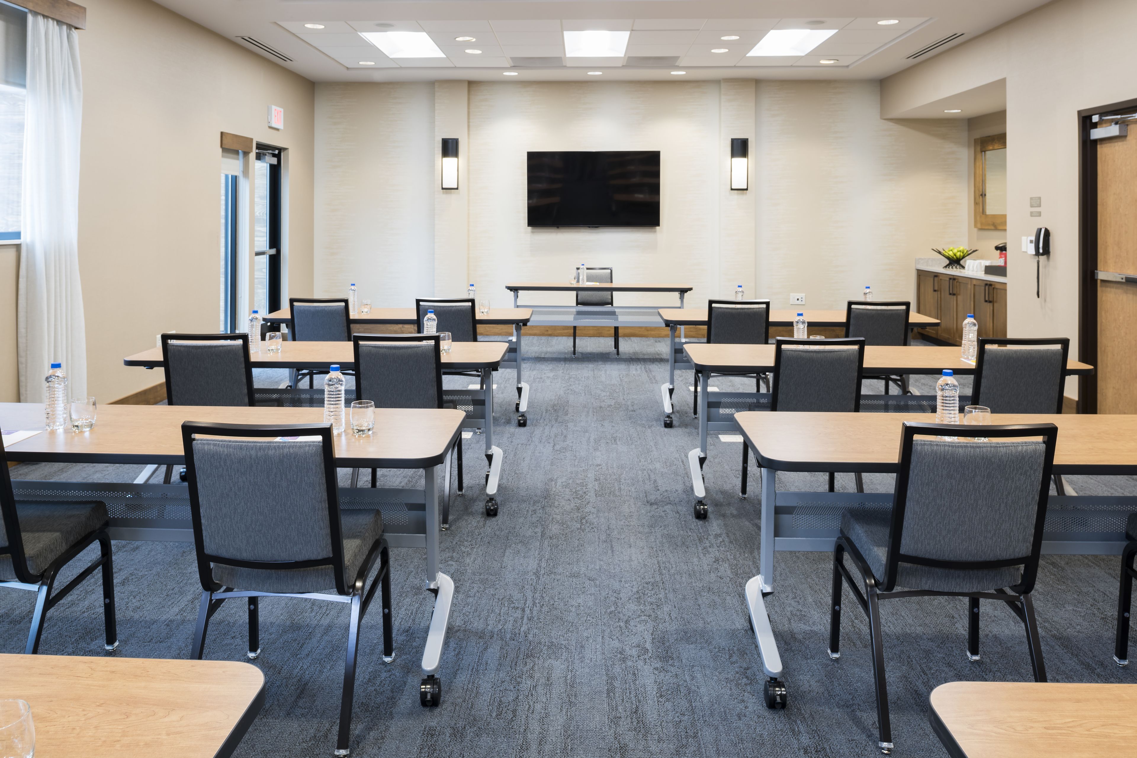 Une salle de conférence équipée d’un grand téléviseur à écran plat, de plusieurs tables avec des chaises et d’un sol recouvert de moquette.