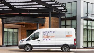 A white van parked in front of a modern building with a glass facade and a covered entrance.