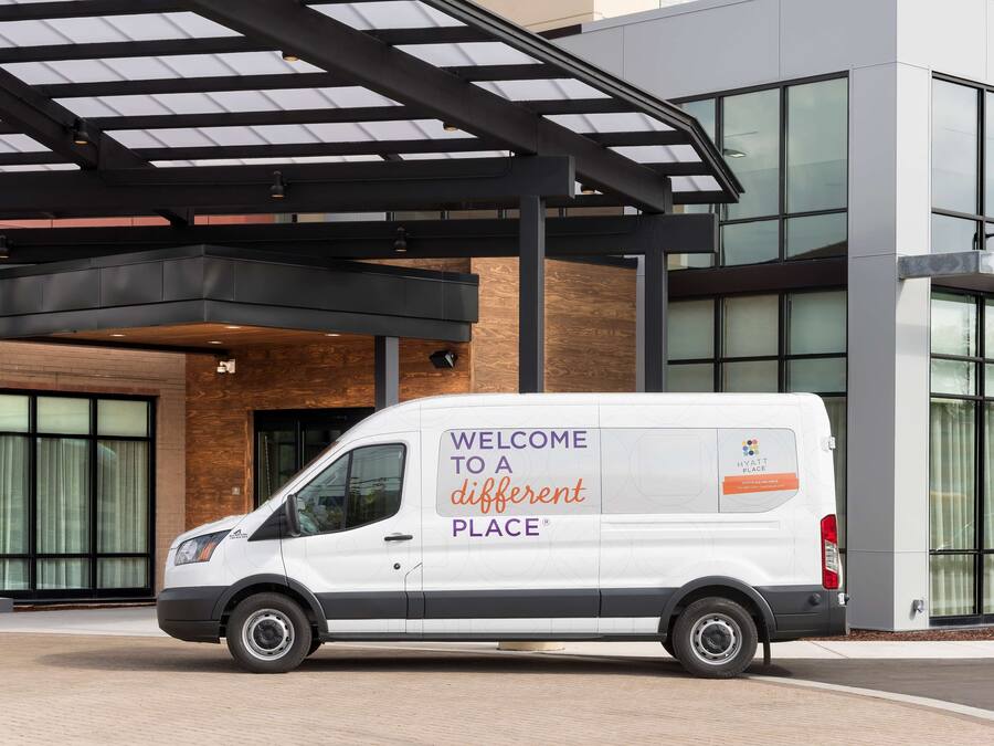 A white van parked in front of a modern building with a glass facade and a covered entrance.
