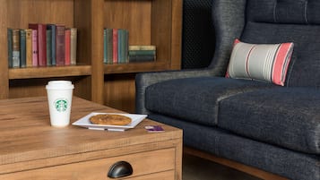 A cozy seating area with a wooden coffee table, a white plate with a cookie, a Starbucks cup, and a smartphone.