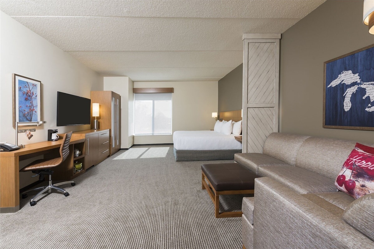 A hotel room with a bed, a desk with a chair, a sofa, a TV, and a window.