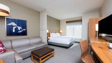 A hotel room with a bed, a sofa, a wooden table, a TV, and a painting on the wall.