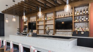 Una zona de bar con una barra alargada, diversas opciones de asientos y estanterías llenas de botellas y vasos.