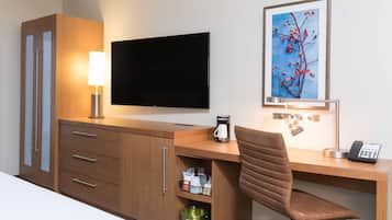 A hotel room with a wooden desk, a flat-screen TV, a coffee maker, a phone, and a framed picture on the wall.