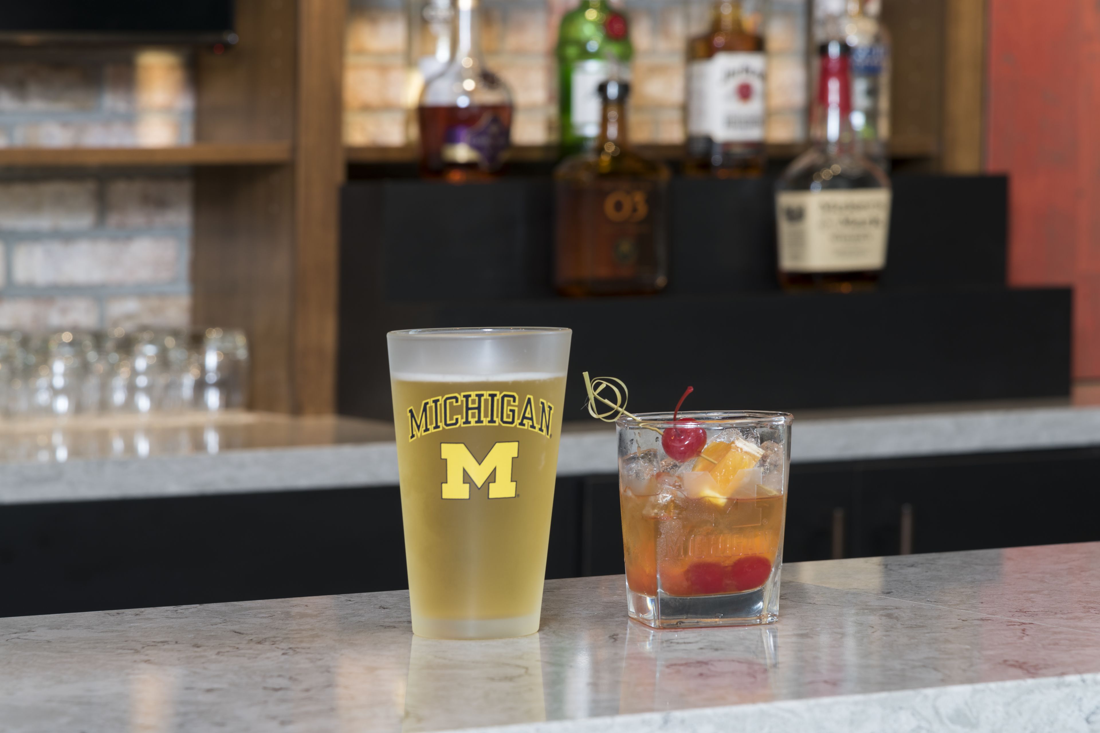 Un bar con un vaso con motivos de Michigan, un cóctel con fruta y una cereza.