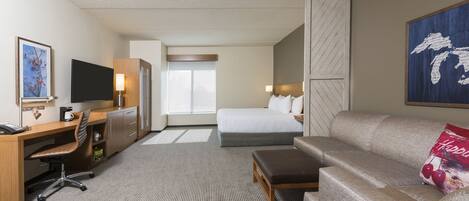 A hotel room with a bed, a sofa, a desk with a chair, a TV, and a window.