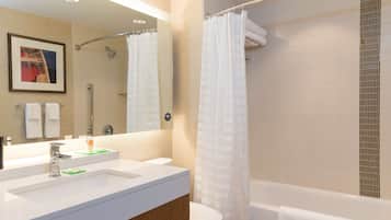 A modern bathroom with a white sink, mirror, and toilet. A shower curtain is visible, and a towel is hung on the bathtub.