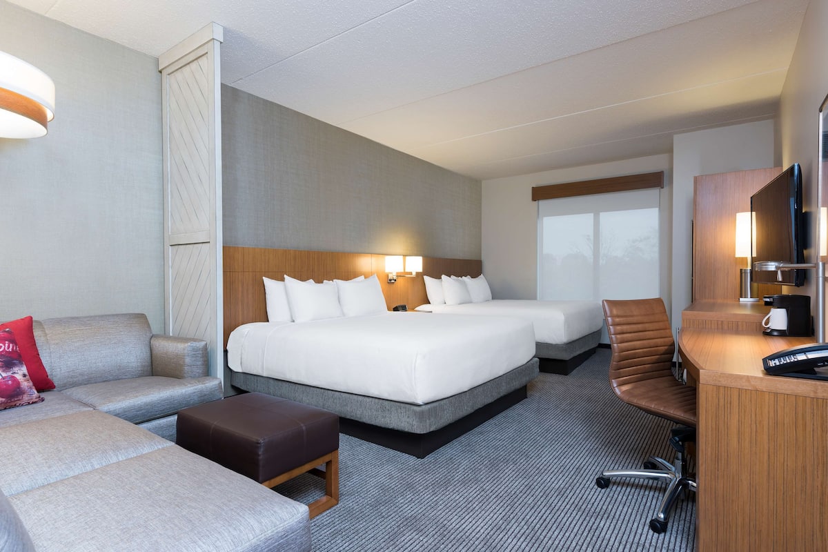 A hotel room with two beds, a sofa, a desk, and a TV.