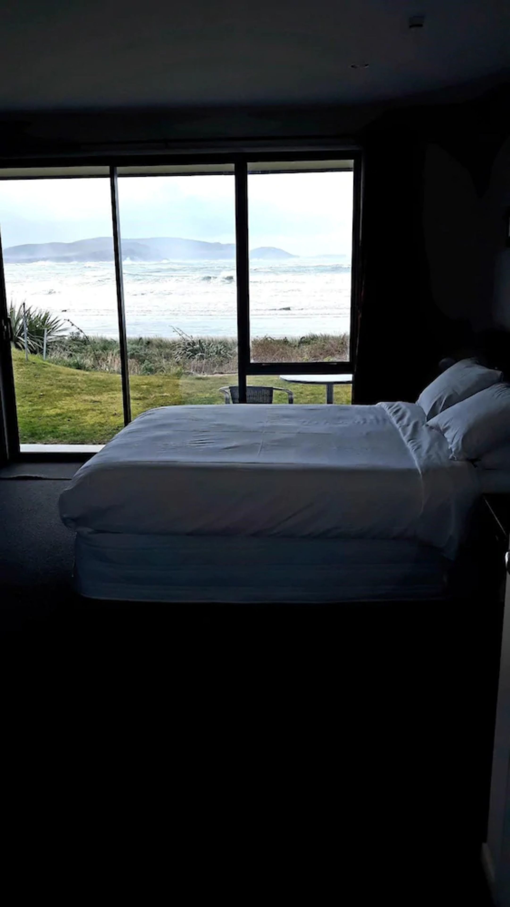 A bedroom with a large window offering a view of the ocean and hills.