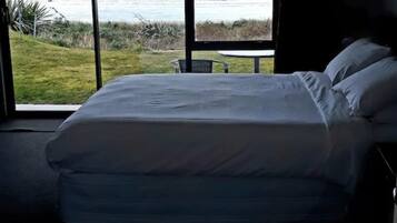 A bedroom with a large window offering a view of the ocean and hills.