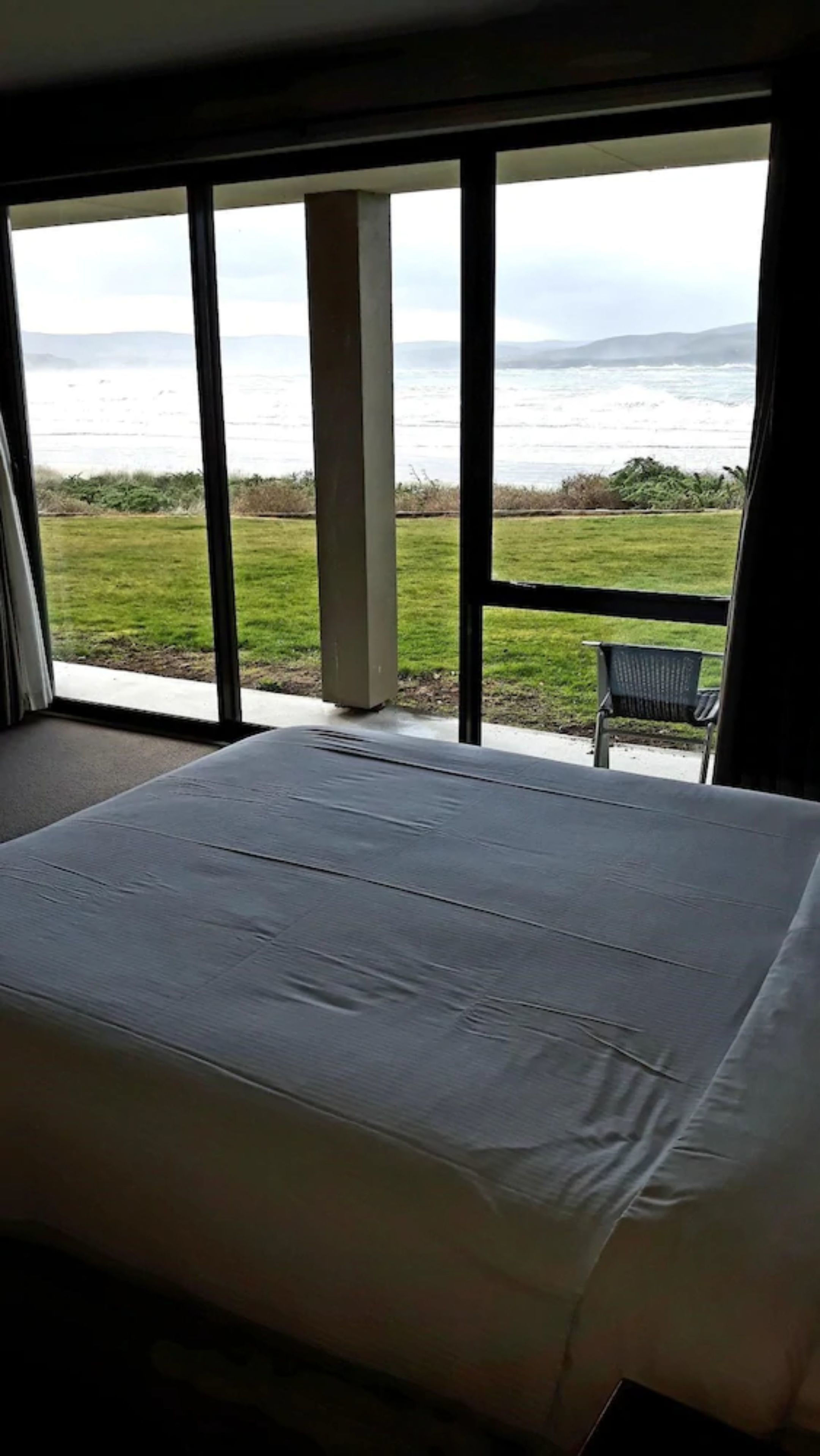 Un dormitorio con una cama grande, vista al océano y una silla junto a la ventana.