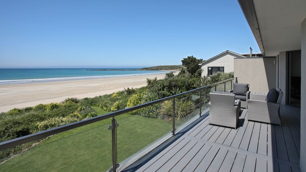 A balcony with wicker furniture overlooking a beach.