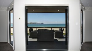 A room with a large sliding glass door leading to a balcony with a view of the ocean and hills.