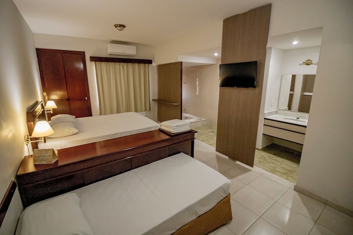 A hotel room with a bed, bedside table, lamp, and a bathroom with a mirror and sink.