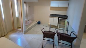 Un ambiente compatto con angolo cottura, un tavolo in vetro e sedie, zona doccia e piccolo bagno.