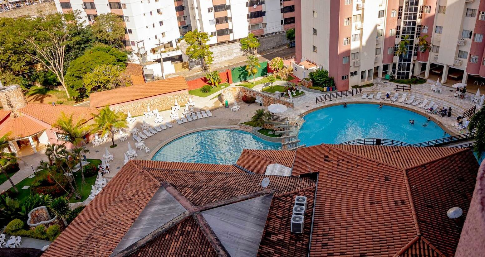A rooftop pool area with multiple swimming pools, lounge chairs, and a view of surrounding buildings.