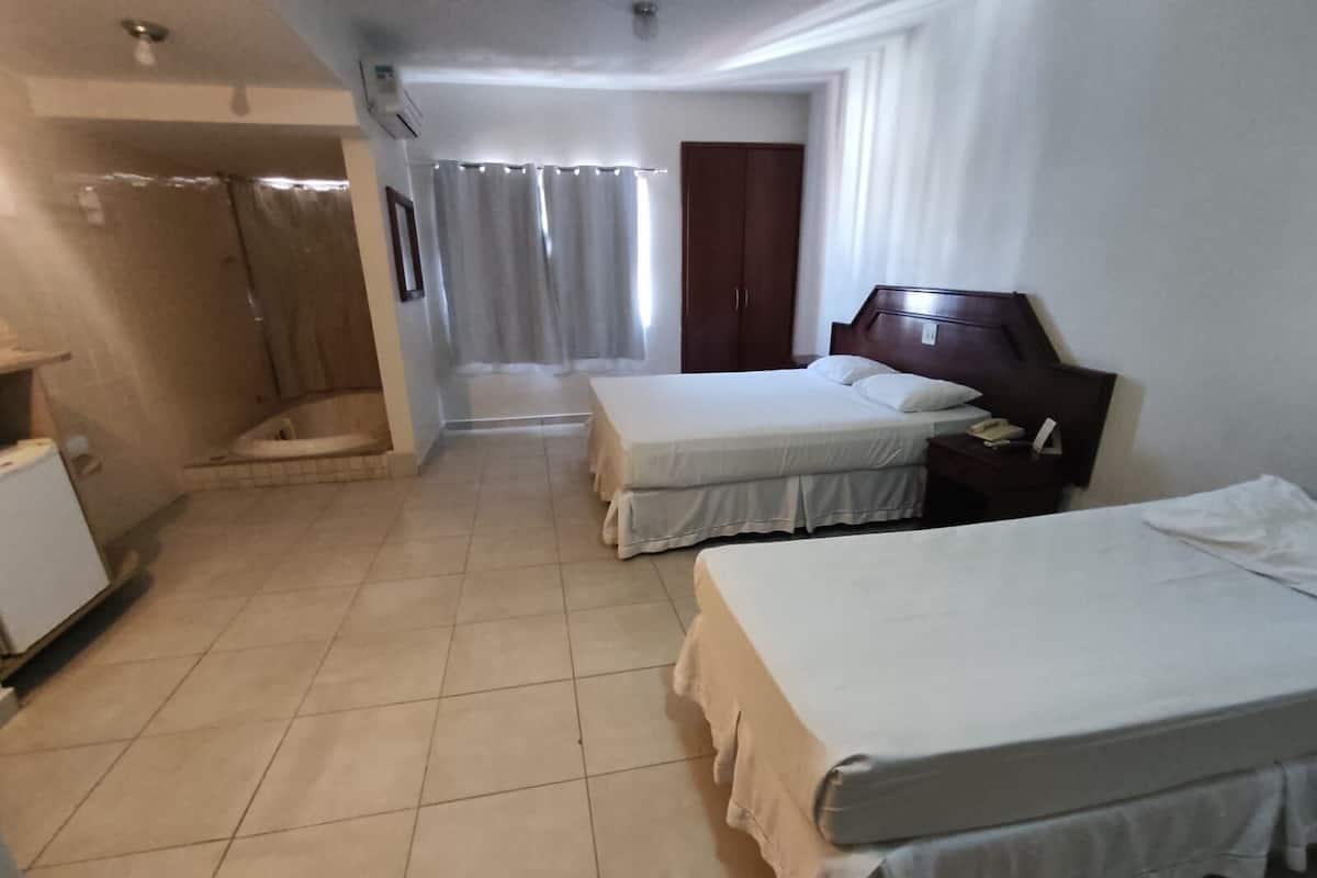 A hotel room with two beds, a shower, a small table, and a wardrobe.