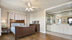 Un dormitorio con una cama de madera, un ventilador de techo, una mesita de noche, un aparador y un espejo grande.