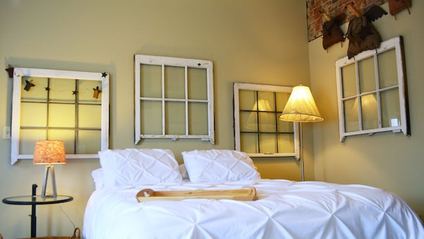 Een net opgemaakt bed met witte lakens, een houten bedloper en een lamp op een nachtkastje.