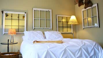 A neatly made bed with white linens, a wooden bed runner, and a lamp on a bedside table.