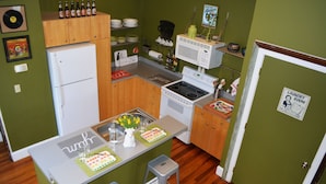 Een kleine keuken met een koelkast, fornuis, magnetron en houten kastjes. Er is een zithoek met een tafel en stoelen.