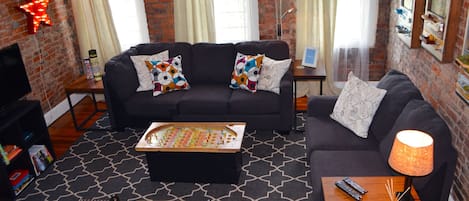 A cozy living room with a black sofa, patterned cushions, a coffee table, and a lamp.