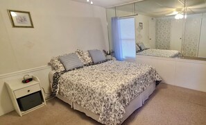 Une chambre à coucher avec un lit, une table de chevet, un miroir et une fenêtre avec des stores.