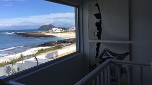 Een balkon met uitzicht op een strand, een rotsachtige kustlijn en een berg in de verte.