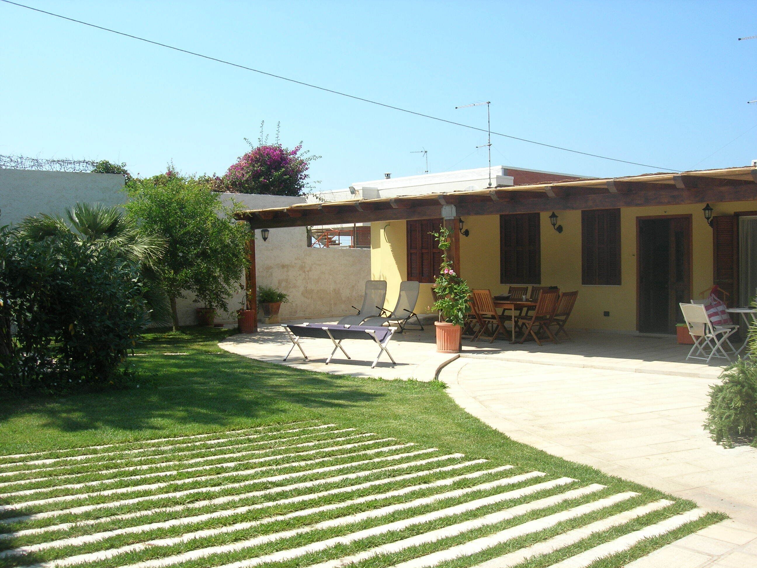 A patio with outdoor seating, a small garden, and a building with yellow walls and a roof.