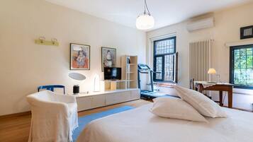 Un dormitorio moderno con una cama grande, un escritorio con ordenador, una silla y una obra de arte en la pared.