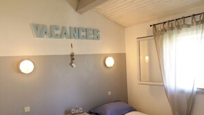A bedroom with two beds, a nightstand, a wall-mounted light, and a sign that reads "VACANCES". - Rare and typical holiday house 400 m from the beach !!! (Agde)