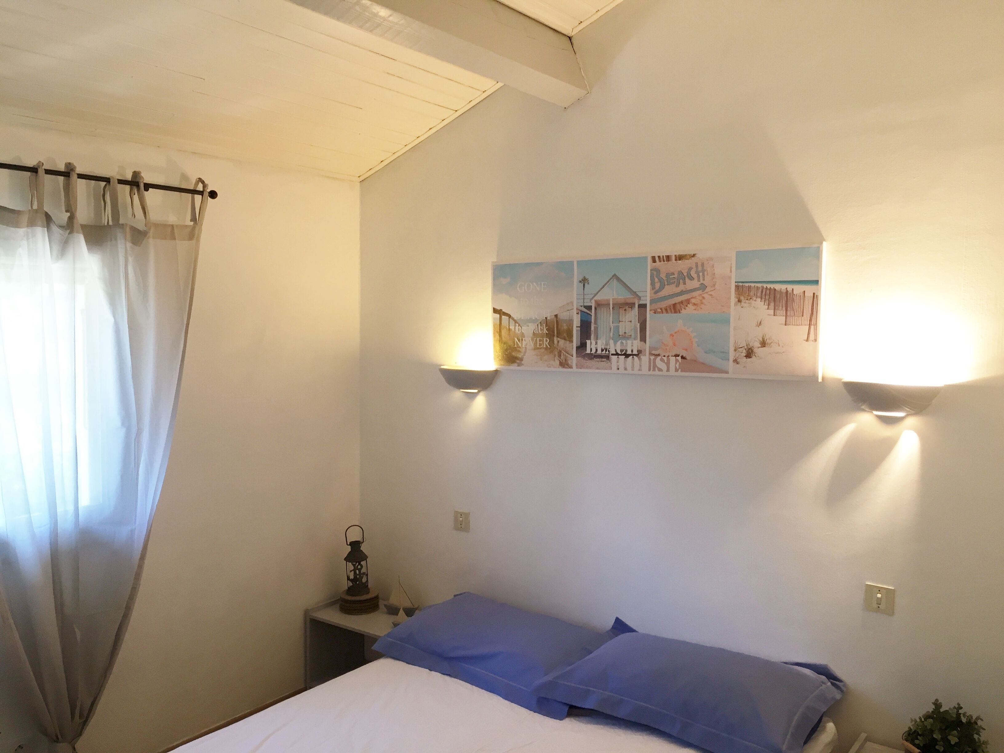 A bedroom with a bed, a nightstand, a lamp, a wall with pictures, and a window with curtains.