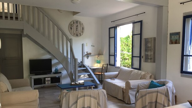 A living room with a staircase, a television, a clock, and a window with shutters. - Rare and typical holiday house 400 m from the beach !!! (Agde)