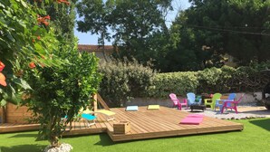 A wooden deck with colorful chairs and a table, surrounded by green grass and trees. - Rare and typical holiday house 400 m from the beach !!! (Agde)