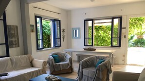 A spacious living room with a white sofa, two armchairs, a coffee table, and a dining table. Large windows provide natural light and views of greenery outside. - Rare and typical holiday house 400 m from the beach !!! (Agde)