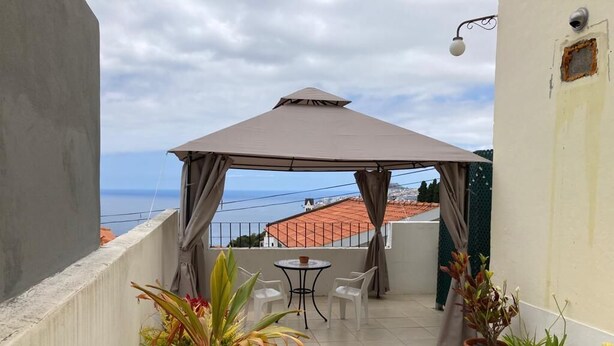 Ein Balkon mit Tisch und Stühlen, Blumentöpfen und Blick aufs Meer.