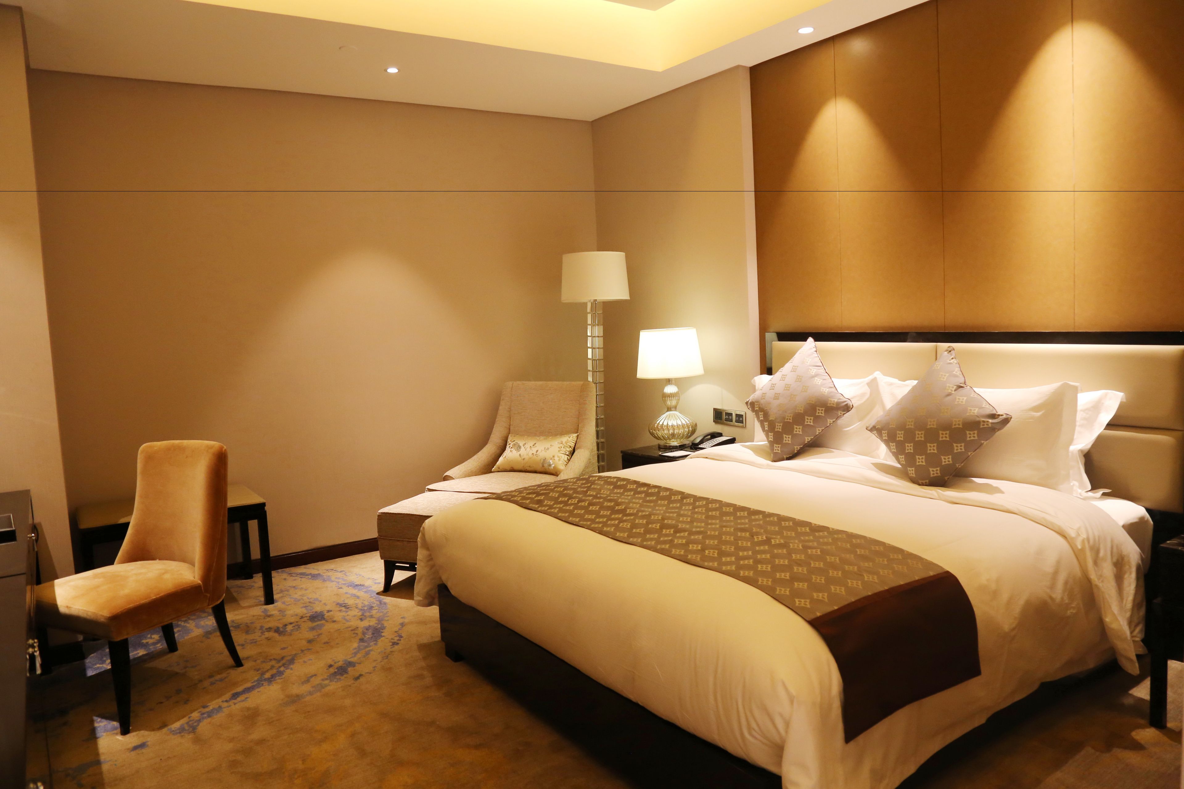 Una habitación de hotel con una cama grande, una silla, una mesita de noche y una lámpara.