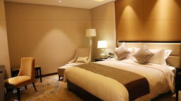 Una habitación de hotel con una cama grande, una silla, una mesita de noche y una lámpara.