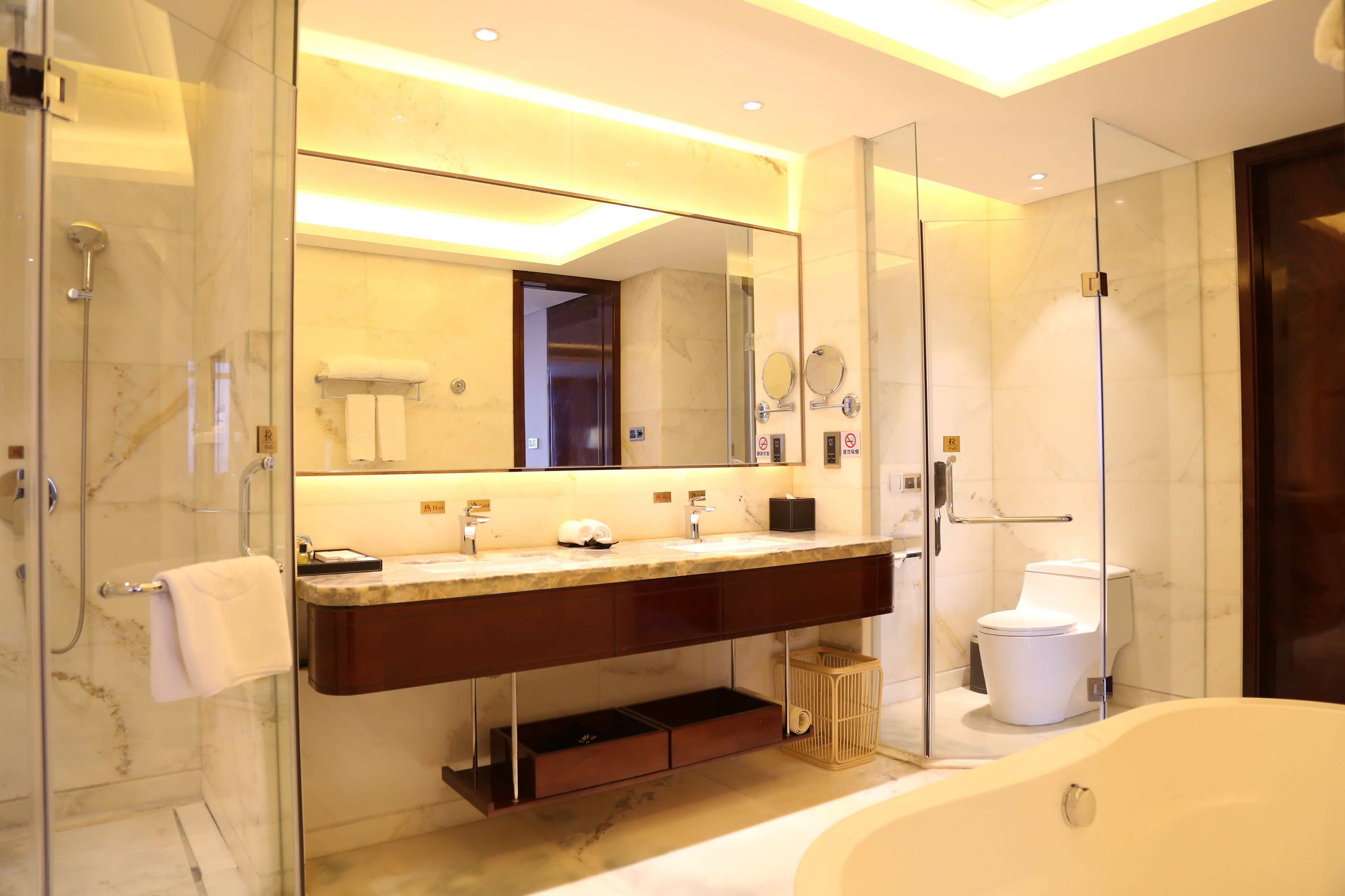 Un baño moderno con ducha envuelta en vidrio, lavabo de mármol, espejo grande y bañera independiente.
