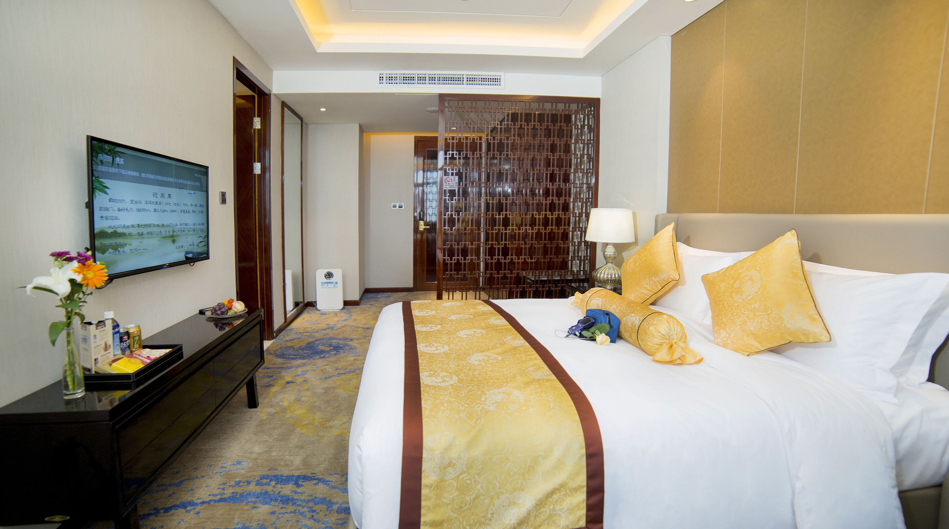 A hotel room with a bed, a desk, a TV, and a decorative screen displaying text.
