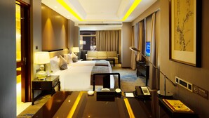 Une chambre d’hôtel avec un grand lit, des tables de chevet, un bureau, une chaise, une lampe, une télévision et un tableau au mur.