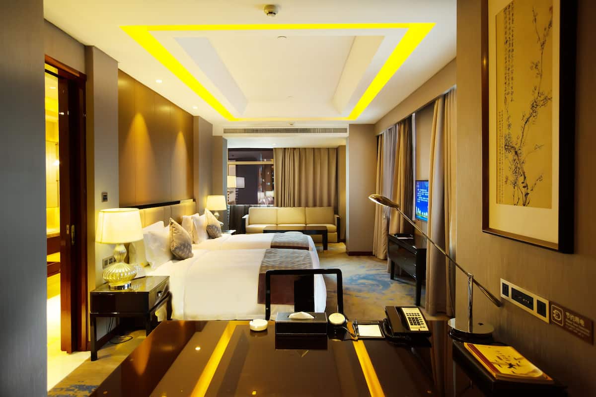 Quarto de hotel com uma cama grande, mesas de cabeceira, escrivaninha, cadeira, luminária, televisão e um quadro na parede.
