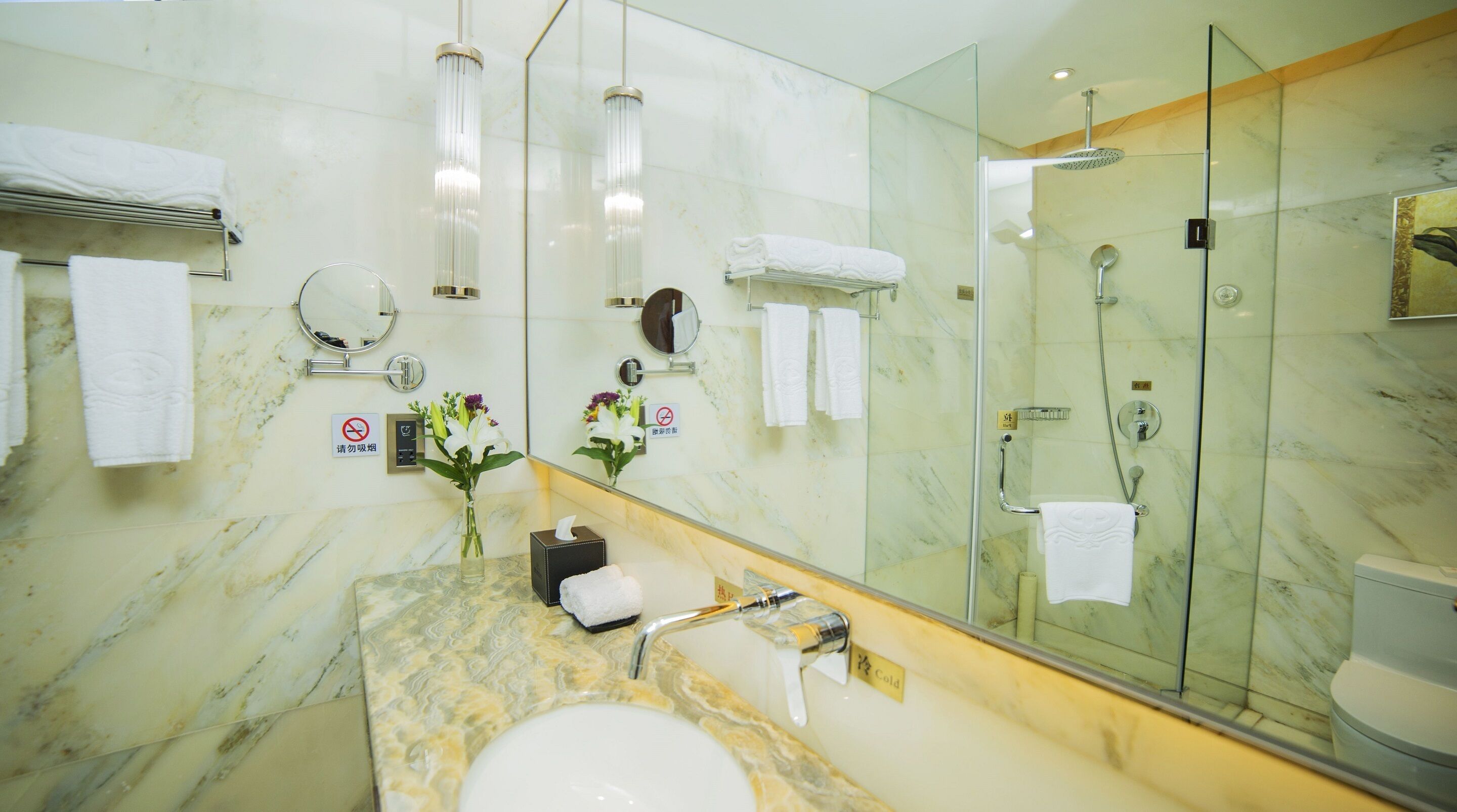 Un baño moderno con lavamanos de mármol, cabina de ducha con mampara de vidrio y un espejo grande.