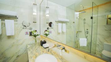 Un baño moderno con lavamanos de mármol, cabina de ducha con mampara de vidrio y un espejo grande.