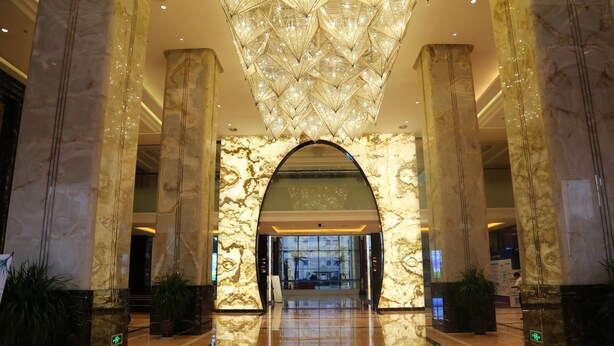 Un vaste hall d’entrée orné de colonnes en marbre, d’un grand lustre et d’un sol réfléchissant.